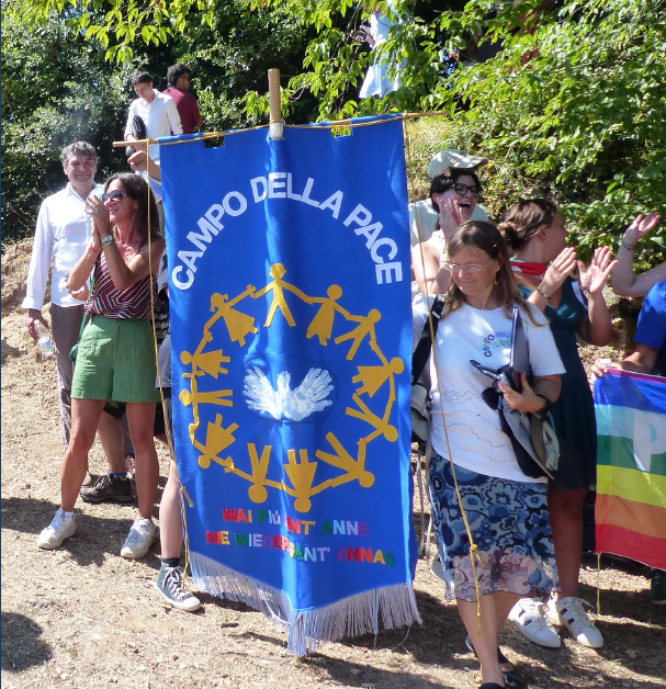 Petra Quintini und Teilnehmende des Campo della Pace mit dem blaen Banner des Campo della Pace bei der Gedenkfeier am 12.8.2024