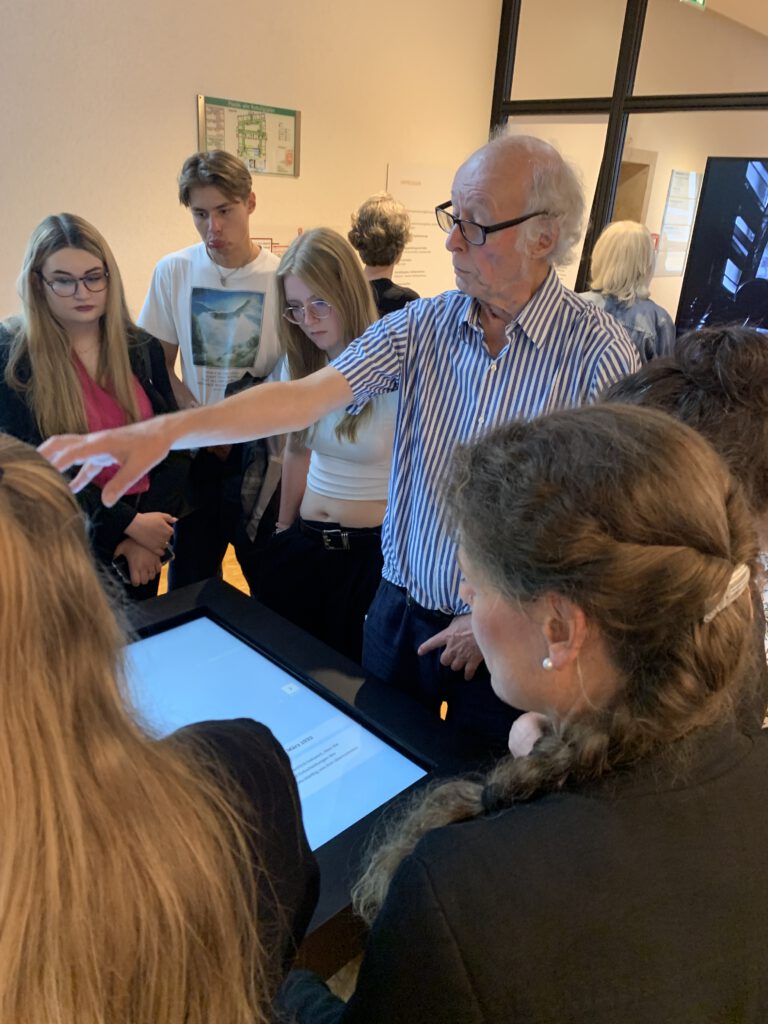 Harald Stingele an der Medienstation, ein Lichttisch, zeigt und erklärt den Aufbau der Medien. Im Vordergrund: Julianna Herzberg, Schauspielerin und Mitwirlkende im Film, bei den Zuhörenden