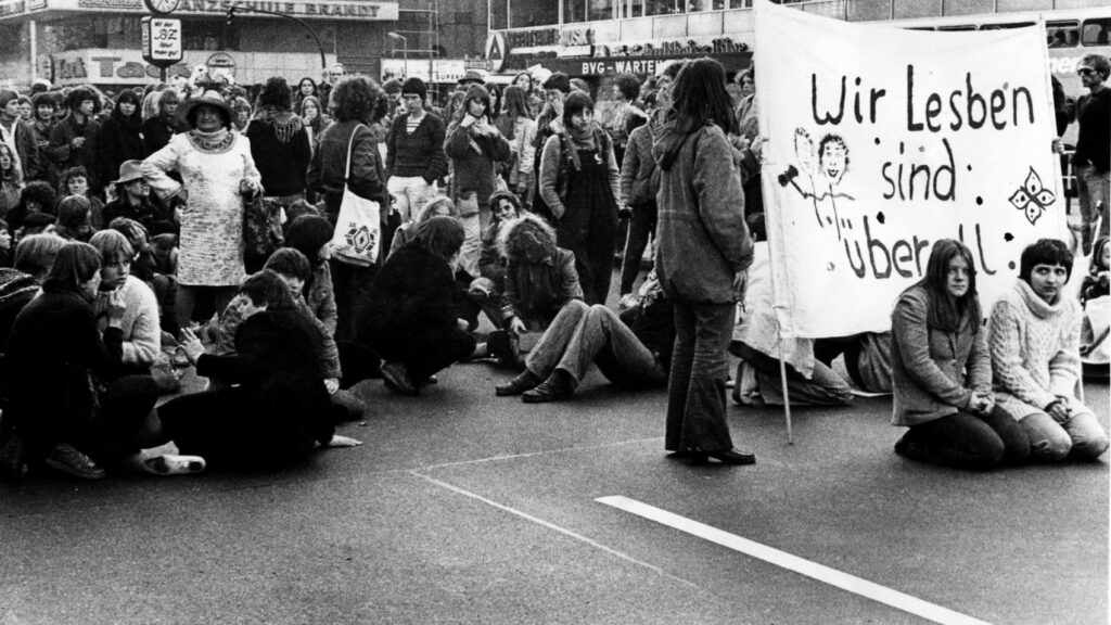 schwarz7weiß-BildSitzblockade von Frauen sitzend und stehend hinter einem Transparent mit der Aufschrift"WirLesben sind überall)